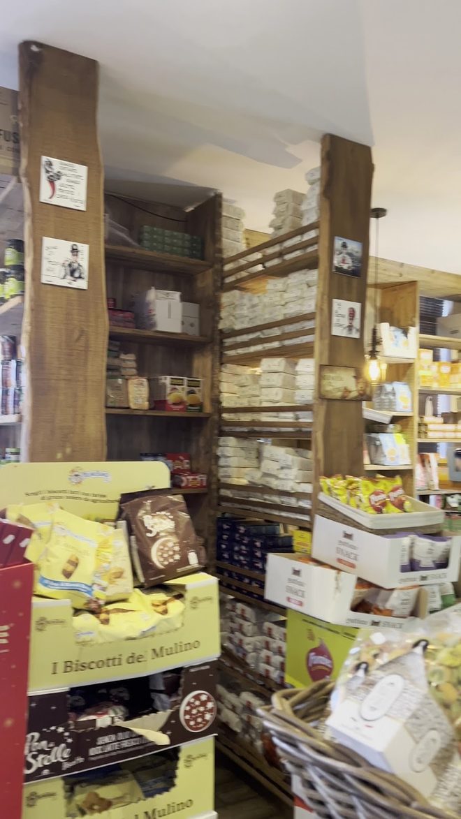 A narrow aisle of wooden shelving stocked with Italian biscuits and groceries